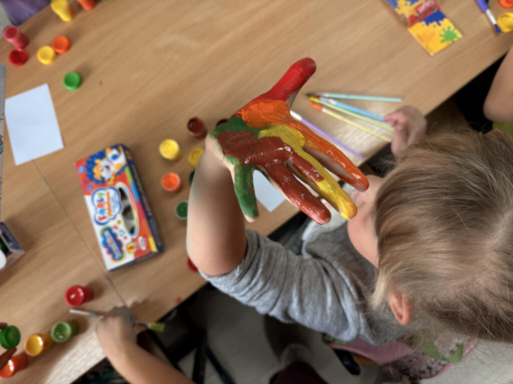 Dziecko ma dłoń wymalowaną farbą w kolorach jesiennych.