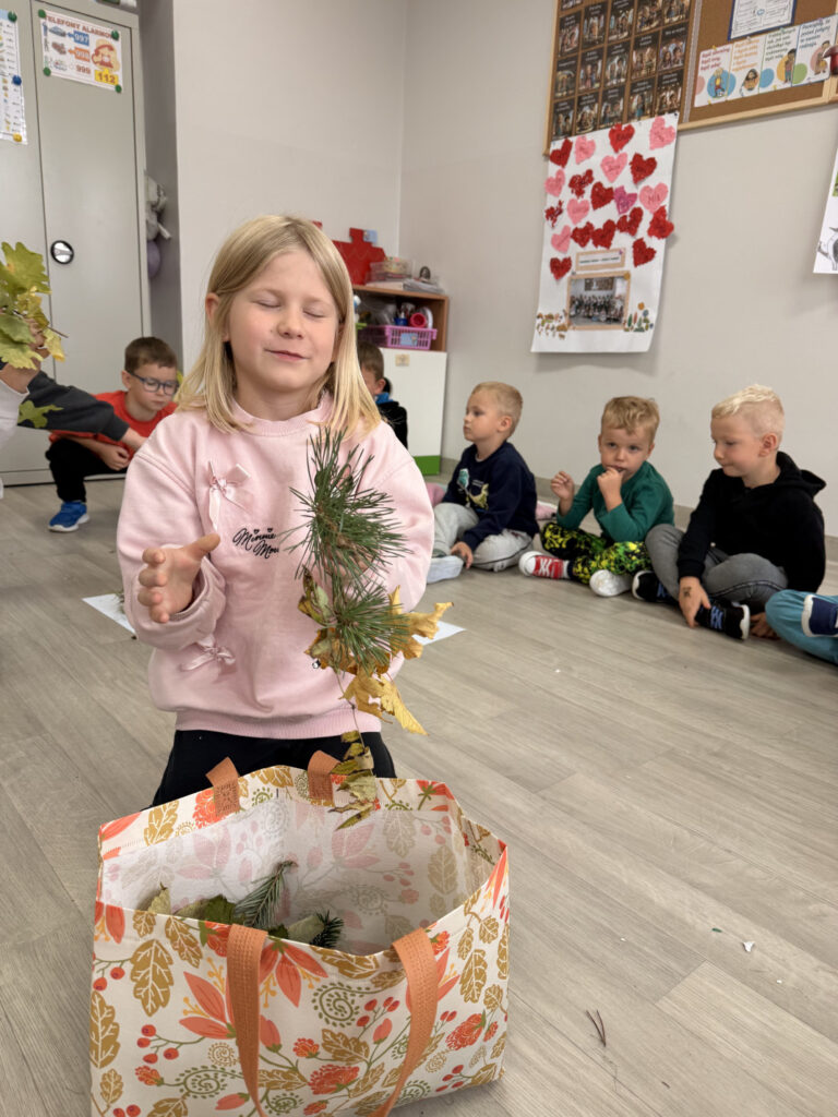 Zdjęcie przedstawia dziewczynkę wyciągającą zagadkę sensoryczną z torby pełnej sensorycznych, naturalnych darów Ziemi.
