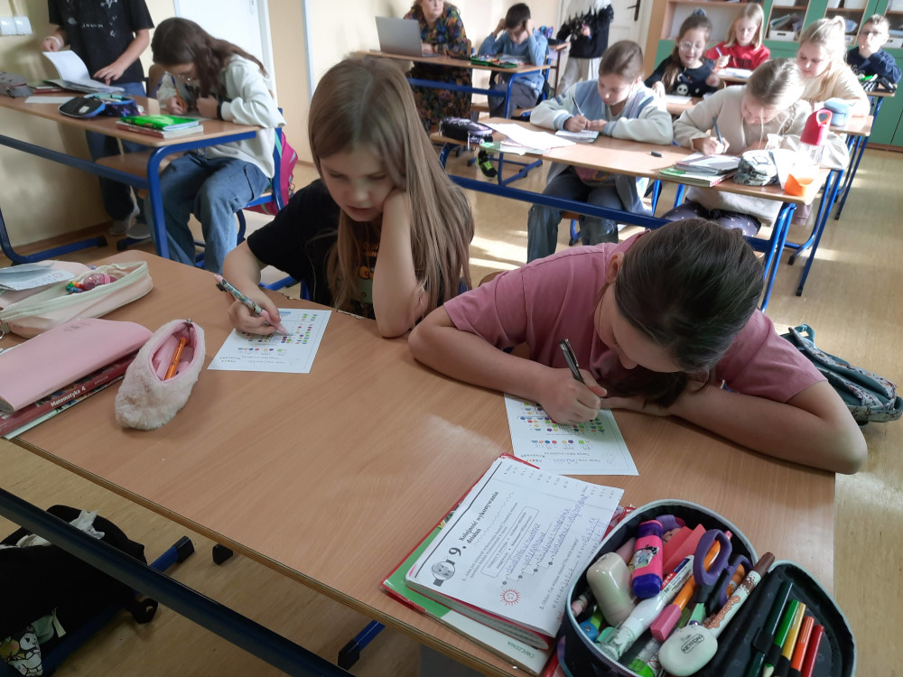 Uczniowie w szkolnej klasie siedzą przy ławkach i samodzielnie wypełniają karty pracy z zadaniami logicznymi.