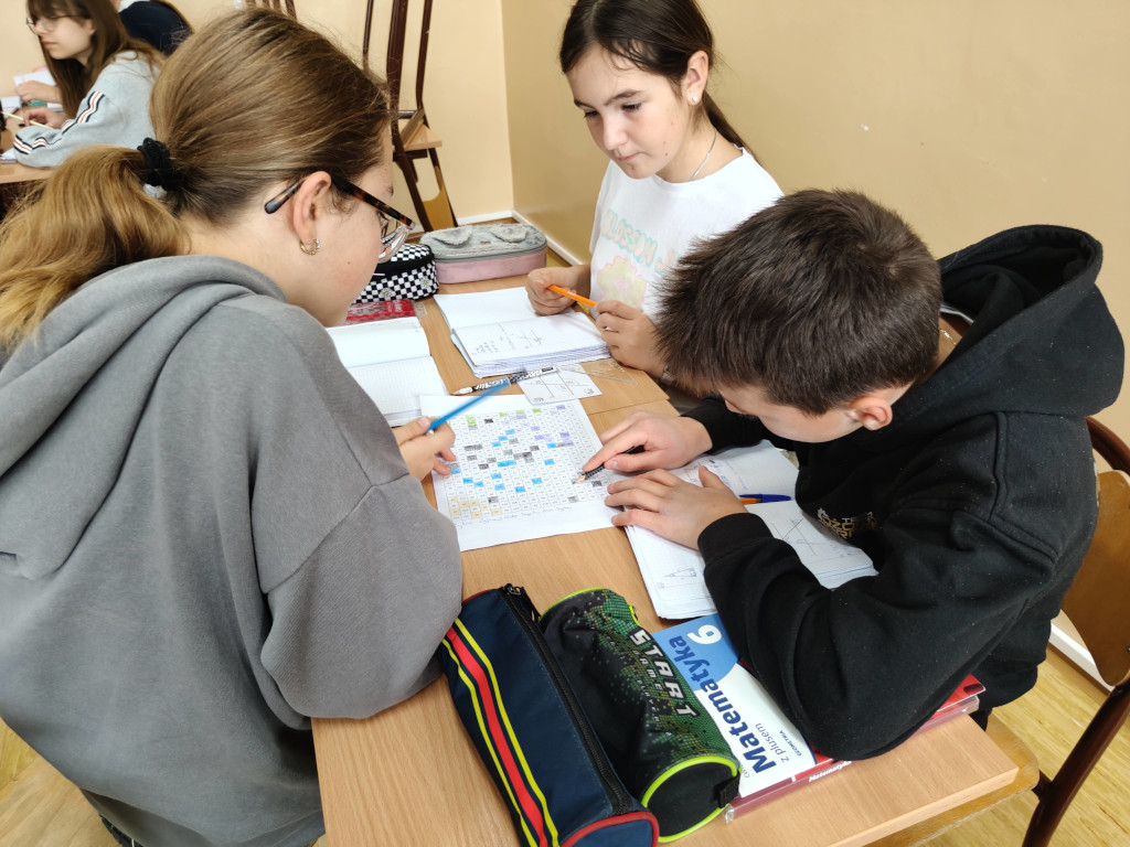 Troje uczniów skupia się na wspólnym rozwiązywaniu zadań geometrycznych i uzupełnianiu karty z zakodowanym obrazkiem.
