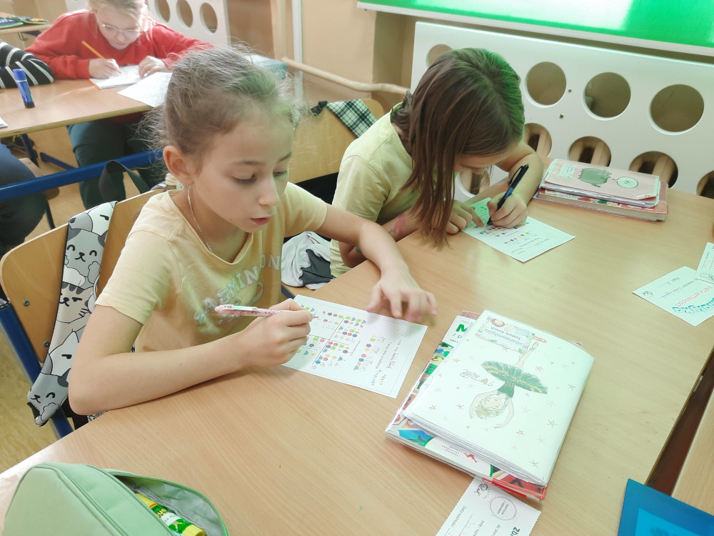 Dwie dziewczynki siedzące w ławce skupiają się na rozwiązywaniu zadań matematycznych z figurami.