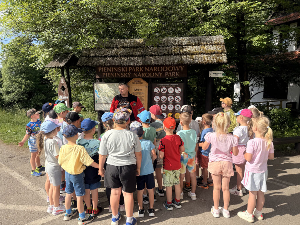 Dzieci słuchają ciekawostek przekazanych przez przewodnika o przyrodzie Parków Narodowych.