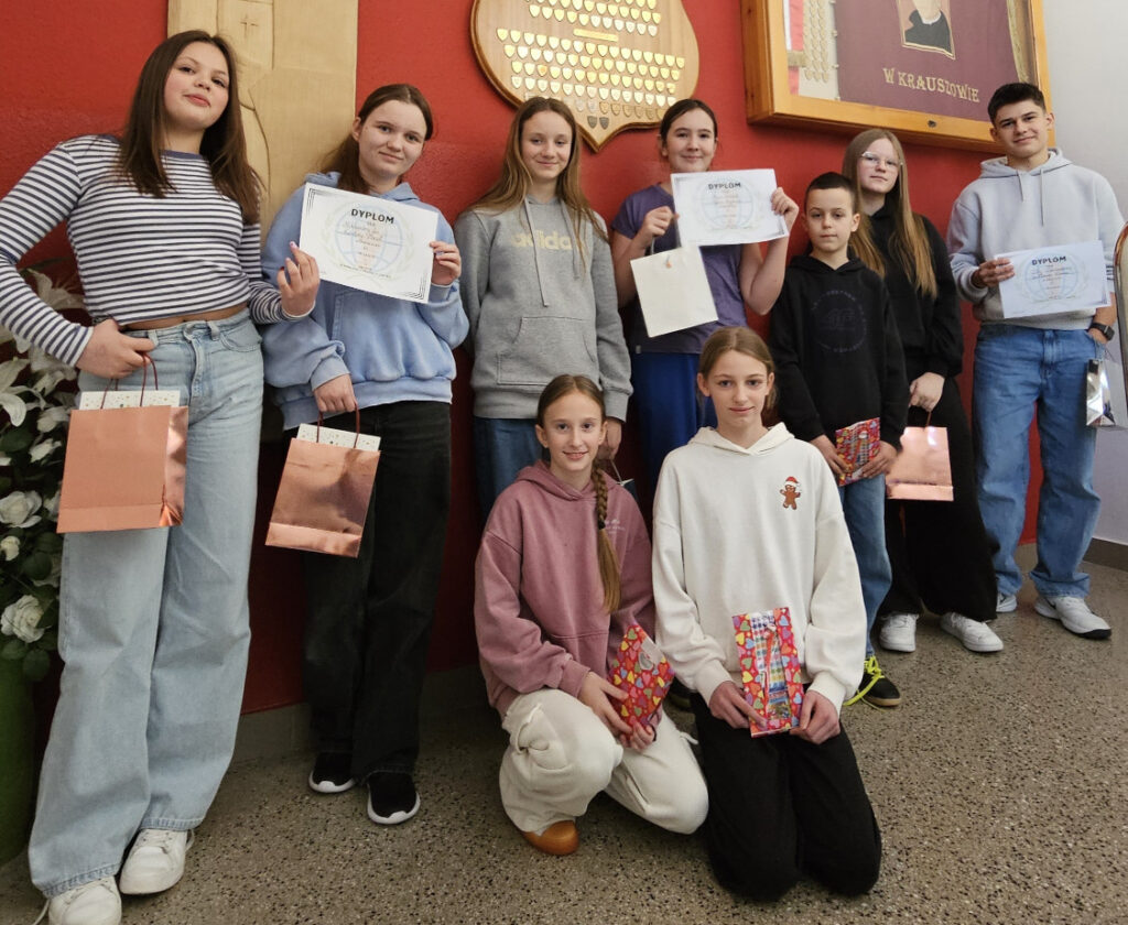 Grupa dziewięciorga uśmiechniętych uczniów prezentuje otrzymane dyplomy i upominki na tle czerwonej ściany