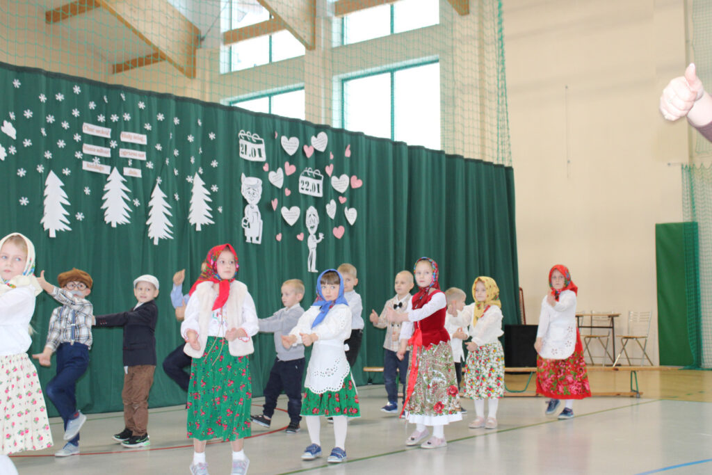 Dzieci ustawione w rzędach wykonują układ taneczny podczas występu w sali gimnastycznej.