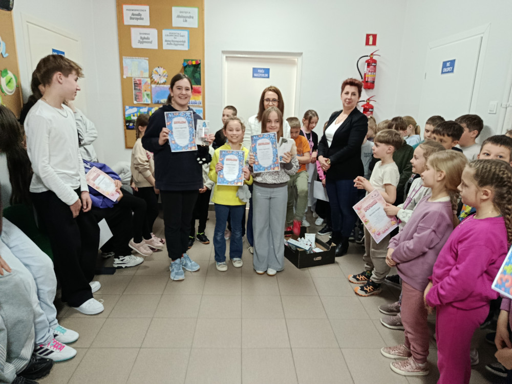 Grupa uczniów dumnie prezentuje otrzymane upominki i nagrody na korytarzu szkolnym.