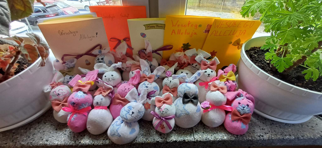 Kolorowe, ręcznie wykonane ozdoby wielkanocne w kształcie króliczków ustawione na parapecie obok doniczek z roślinami i kartek z napisem „Wesołego Alleluja”.