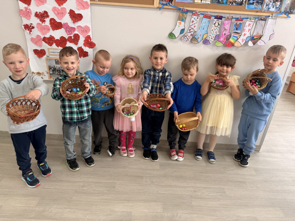 Grupa uśmiechniętych dzieci pozuje do zdjęcia, trzymając przed sobą koszyczki wypełnione czekoladowymi jajkami.