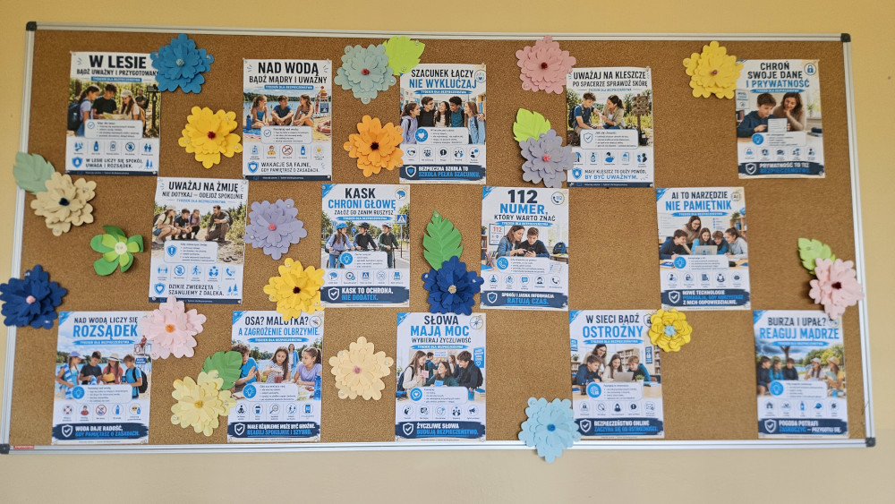 Szkolna gazetka poświęcona zasadom bezpieczeństwa. Składa się z kilkunastu małych plakatów z grafikami i hasłami edukacyjnymi, takimi jak: "W lesie", "Nad wodą", "Uważaj na żmije", "Szacunek łączy", "Kask chroni głowę", "Nad wodą liczy się rozsądek", "Uważaj na kleszcze", "112 numer który warto znać", "Słowa mają moc", "W sieci bądź ostrożny" oraz "Burza i upał". Wolne przestrzenie między plakatami ozdobione są kolorowymi, papierowymi kwiatami.